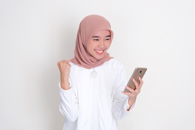 Eine muslimische asiatische Frau zeigt einen glücklichen und aufgeregten Gesichtsausdruck, wenn sie auf ihr Handy schaut