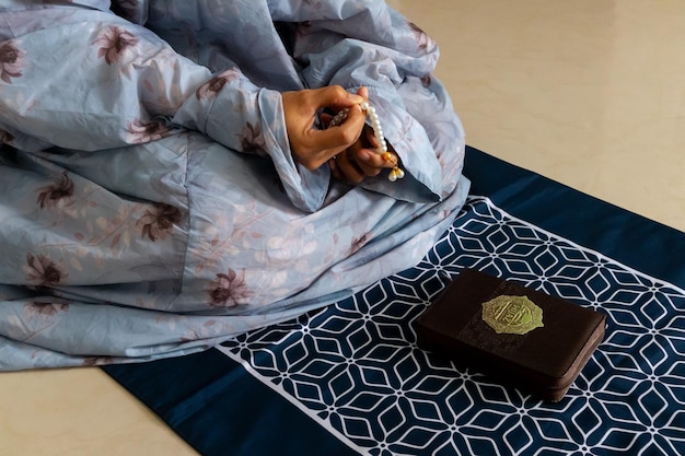Eine muslimische Frau sitzt auf einer Gebetsmatte und hält Gebetsperlen zum Gebet oder Dhikr