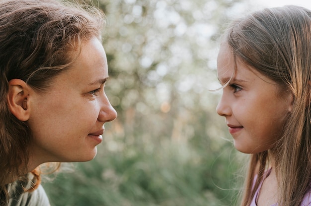 Eine Mutter mit einem kleinen Intra-Channel-Hörgerät kommuniziert mit ihrer kleinen Tochter in der Natur im Freien