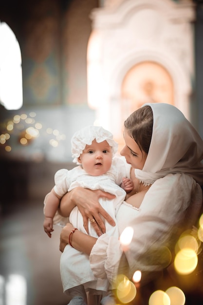 Eine Mutter mit einem kleinen Kind in einem Tempel oder einer Kirche betet neben einer Ikone und Kerzen oder kam zu einem Gottesdienst in der russisch-orthodoxen Kirche zur Taufe eines Babys