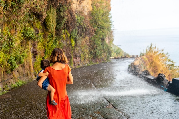 Eine Mutter mit ihrem Sohn in einem roten Kleid am Anjos Wasserfall Madeira