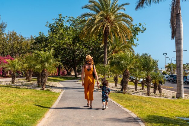 Eine Mutter mit ihrem Sohn spaziert durch Los Cristianos durch einen Park mit Palmen auf der Insel Teneriffa, Kanarische Inseln