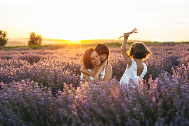 Eine Mutter mit ihren Töchtern bei Sonnenuntergang auf dem Lavendelgebiet bei Sonnenuntergang. Konzept des Internationalen Frauentags