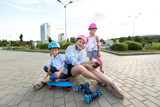 Eine Mutter mit Kindern in Helmen sitzt auf einem Skateboard und spielt im Park mit einem Roboterauto, das von einem Handschuh gesteuert wird.