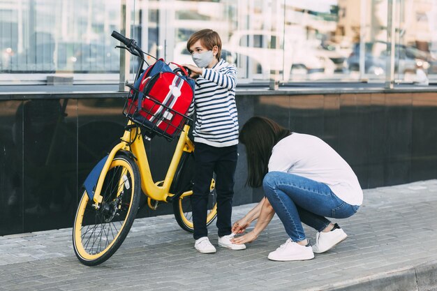 Foto eine mutter passt die stiefel ihres sohnes an, bevor sie mit dem fahrrad zur schule fährt. ein junge trägt eine maske.