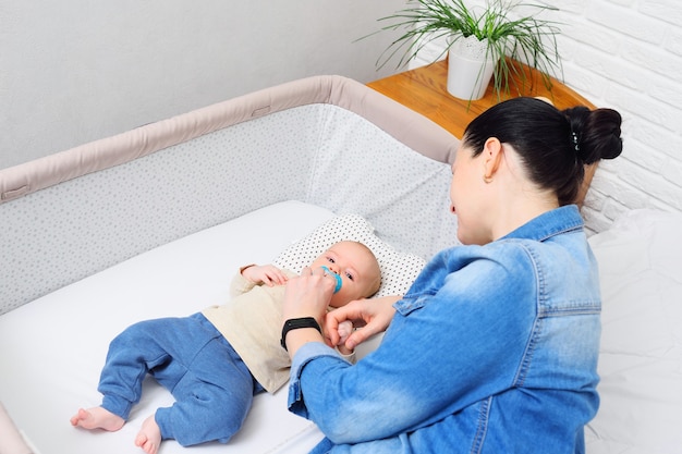 Eine Mutter spielt mit einem Baby, das in einem Beistellbett für ein Neugeborenes oder in einem modernen Laufstall liegt