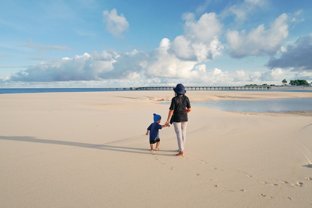 Eine Mutter und ein Sohn gehen am Strand vor dem Pier spazieren.