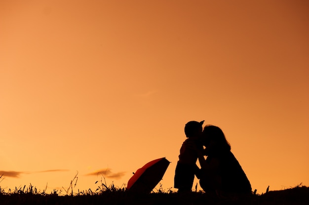 Eine Mutter und ein Sohn mit Regenschirm und draußen spielen bei Sonnenuntergang