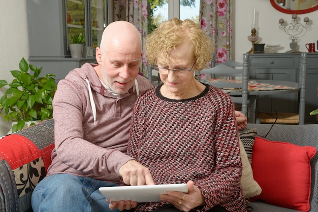 Eine Mutter und ihr erwachsener Sohn, die eine digitale Tablette auf einem Sofa betrachten