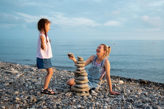 Eine Mutter und Tochter 6 Jahre alt am Strand bauen eine Burg aus Steinen Sommerferien