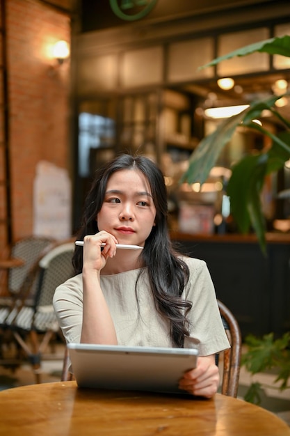 Eine nachdenkliche asiatische Frau denkt nachdenklich über ihre Arbeit nach, während sie sich in einem Café entspannt