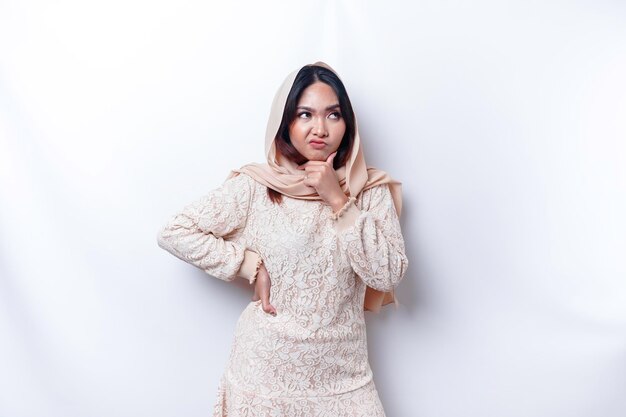 Foto eine nachdenkliche junge asiatische muslimische frau, die hijab trägt, während sie isoliert von einem weißen hintergrund zur seite schaut