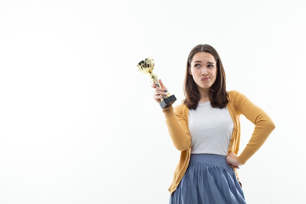 Eine nachdenkliche junge Frau hält einen Goldpokal in der Hand Weißer isolierter Hintergrund