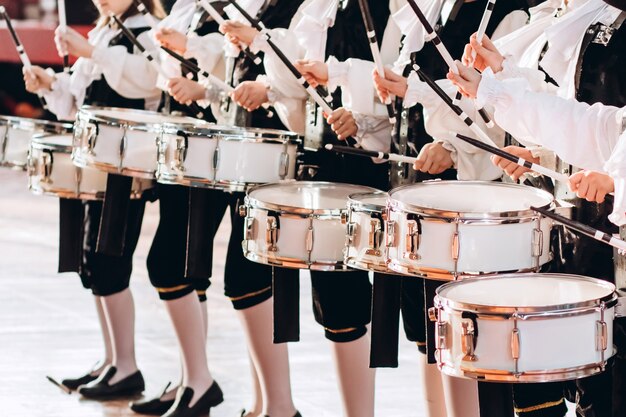 Eine Nahaufnahme der Hände eines Schlagzeugers bei einer Parade. Kinderensemble in weißen Hemden. Weiße neue Snaredrum, weiße Sticks. Das Konzept einer Militärparade und eines Marsches.