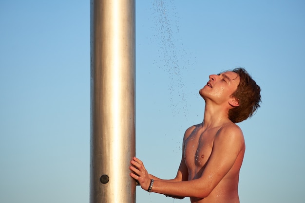 Eine Nahaufnahme des Trinkwassers des jungen Mannes aus einer Dusche am Strand.