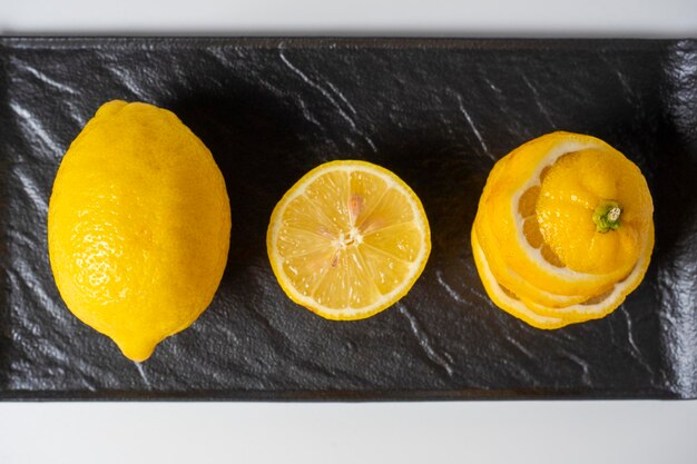 Eine Nahaufnahme einer geschnittenen und ganzen Zitrone liegt auf einem schwarzen strukturierten Teller Weißer Hintergrund Ansicht von oben flach liegend Eine gesunde Zitrusfrucht voller Vitamine