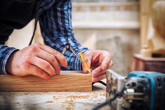 Eine Nahaufnahme eines männlichen Zimmermanns markiert einen Metallkompass und einen Bleistift auf einer Holzstange für die Herstellung von Möbeln