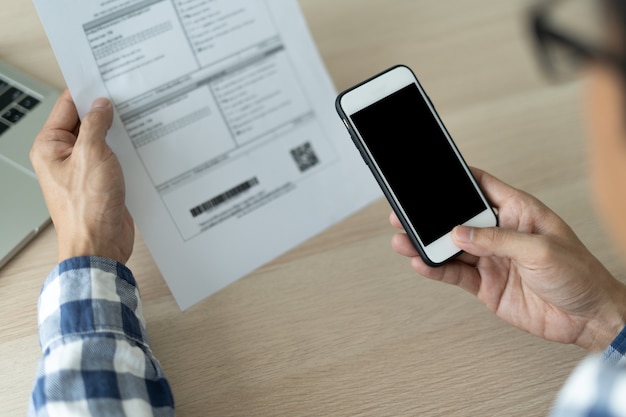 Eine Nahaufnahme eines Mannes, der ein mobiles Smartphone verwendet, um den QR-Code von einer Rechnung auf einem Dokument gegen eine Gebühr zu scannen. Das Konzept der Finanztechnologie, Online-Rückzahlung.