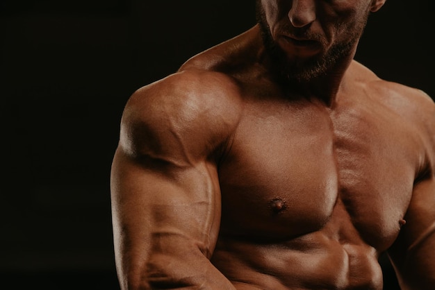 Eine Nahaufnahme eines Torsos eines Bodybuilders mit Bart, der in einem Fitnessstudio Bizeps-Curls macht. Ein Foto eines Teils eines muskulösen Mannes während eines Trainings.