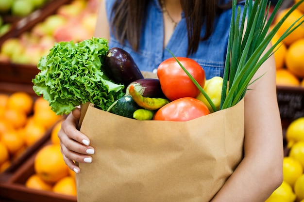 Eine Nahaufnahme Papiertüte mit Gemüse und Obst in weiblichen Händen in den Regalen im Laden