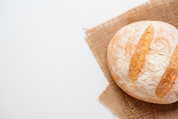 Eine Nahaufnahme von frisch gebackenem Weizenbrot mit knuspriger Kruste liegt auf einem Leinenstoff auf weißem Hintergrund