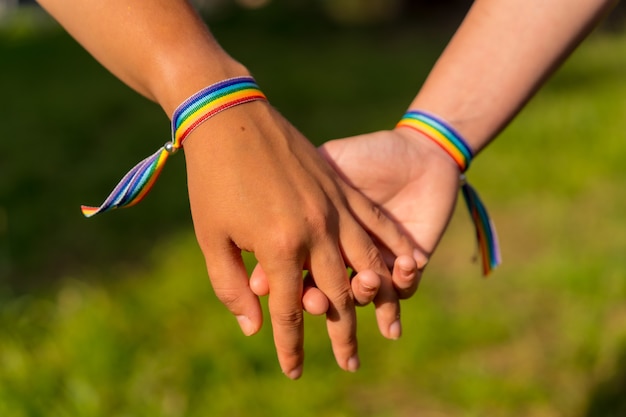 Eine Nahaufnahme von zwei jungen kaukasischen Frauen, die im Freien Händchen mit LGBT-Stolz-Armbändern halten