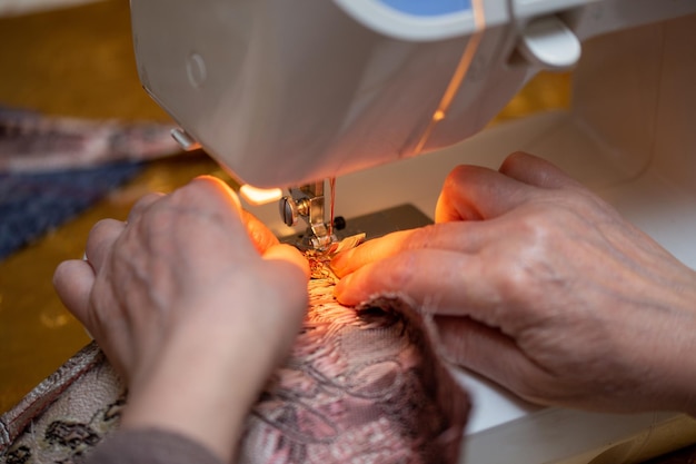 Eine Nahaufnahmeansicht der Nähprozesshand der alten Frau unter Verwendung der selektiven Fokustechnik der Nähmaschine