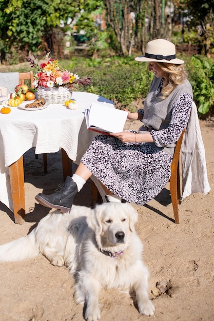 Eine nette Frau mit Hut sitzt an einem Tisch auf der Straße neben einem weißen langhaarigen Labrador