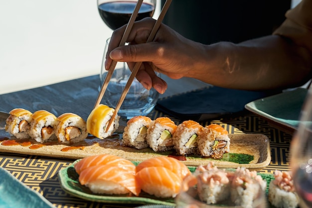 Eine nicht erkennbare Frau nimmt beim Essen in einem asiatischen Restaurant eine appetitliche Sushi-Rolle mit Lachs.