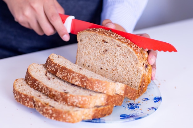 Eine nicht erkennbare Frau schneidet mit einem Messer ein Stück Brot