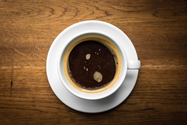 Eine obenliegende Ansicht einer Tasse schwarzen Kaffees auf dem hölzernen Hintergrund, natürliches Licht