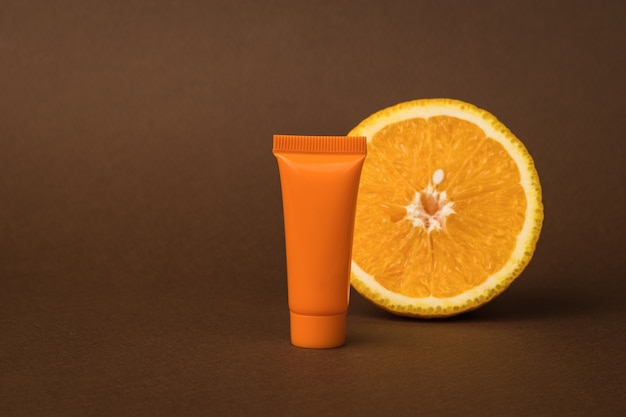 Eine orangefarbene Tube mit Creme und einer Orange auf braunem Grund.