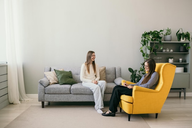 Eine Patientin sitzt auf einem grauen Sofa und erzählt einem Psychologen einer Frau von ihrem Problem. Psychologische Hilfe für Menschen