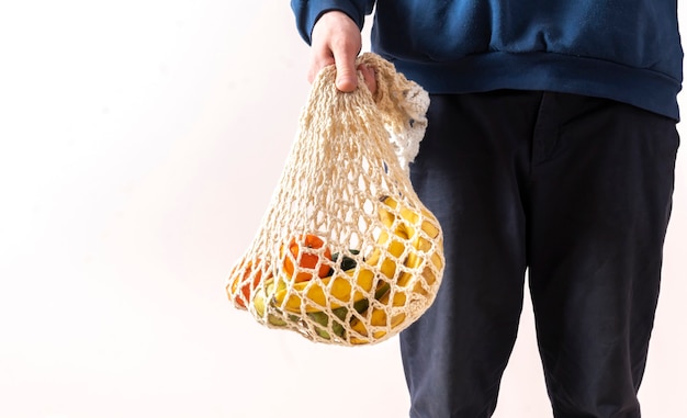 Eine Person, die eine Netztasche mit frischem Rohkostobst und -gemüse hält, umweltfreundliches Zero-Waste-Gespräch