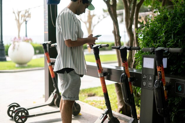 Eine Person, die einen Mietroller nimmt, um sich in der Stadtstraße, Ökologie-Transportmittel, mit Smartphone-App zu bewegen