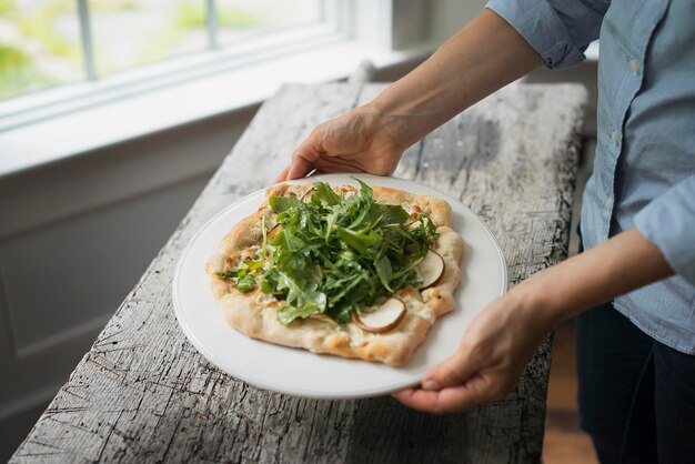 Eine Person, die einen Teller mit frischem Salat und Zutaten auf gebackenem Brot hält