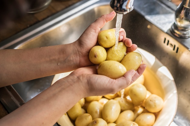 Eine Person, die Kartoffeln unter fließender Wassernahrungsmittelphotographie-Rezeptidee wäscht