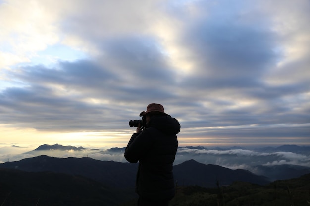 Eine Person fotografiert den Berg gegen einen bewölkten Himmel während des Sonnenaufgangs