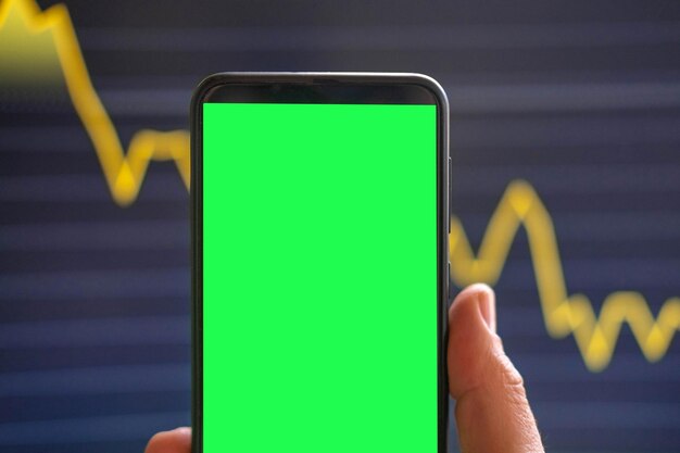 Eine Person hält ein Telefon mit einem grünen Bildschirm, auf dem im Hintergrund ein Diagramm zu sehen ist.