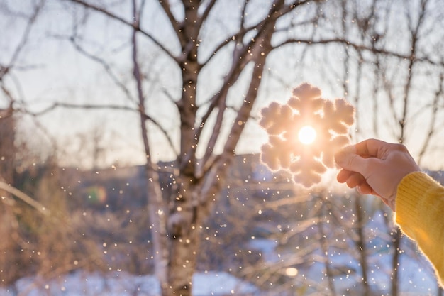 Eine Person hält eine Schneeflocke in der Hand vor einem schneebedeckten Baum.