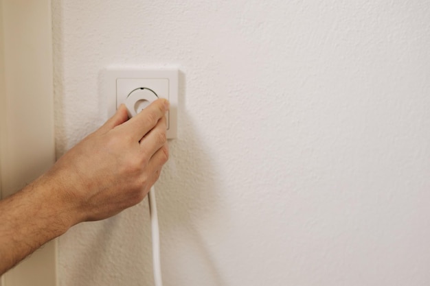 Eine Person hält eine weiße Steckdose mit einem weißen Kabel im Hintergrund.