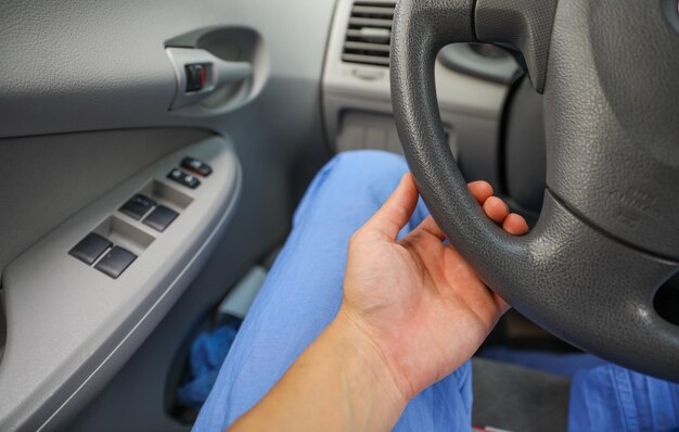 Eine Person in blauen Hosen sitzt in einem Auto und das Lenkrad zeigt die Fahrzeit an.