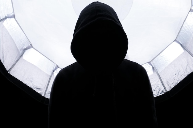 Eine Person in einem schwarzen Hoodie steht vor einem kreisförmigen Fenster mit dem weißen Hintergrund darauf
