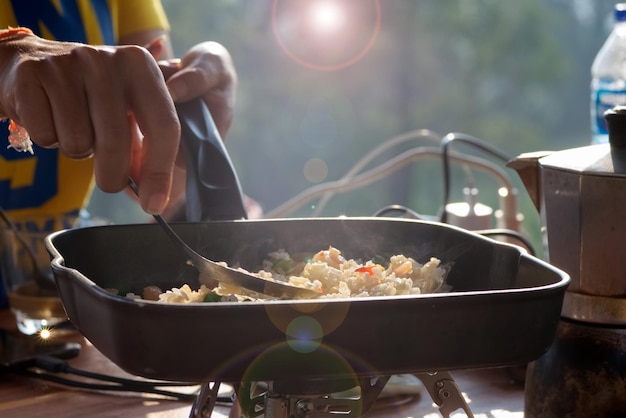 Eine Person kocht morgens gebratenen Reis in einer Pfanne mit unscharfem grünem Feldhintergrund