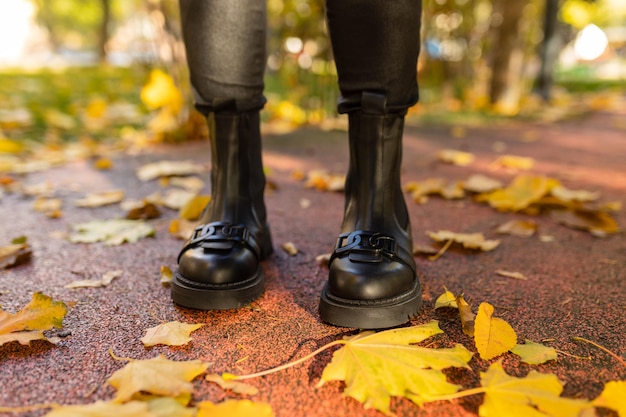 Eine Person mit schwarzen Stiefeln steht auf einem nassen Boden mit Herbstlaub auf dem Boden.