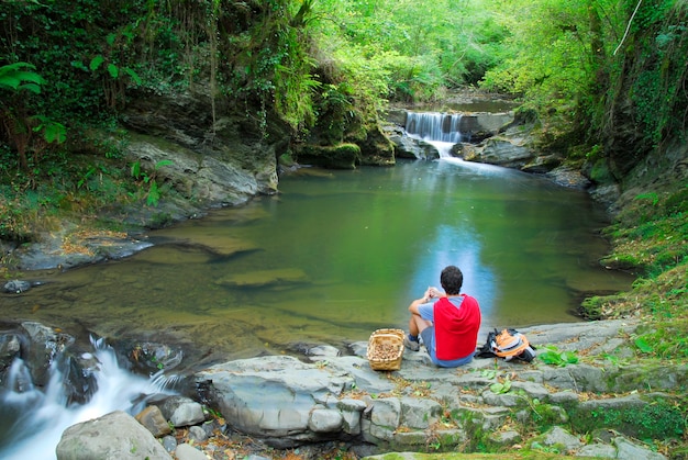 Eine Person ruht neben einem Fluss und einem Wasserfall mit einem Korb Nüsse im Naturpark Gorbeia