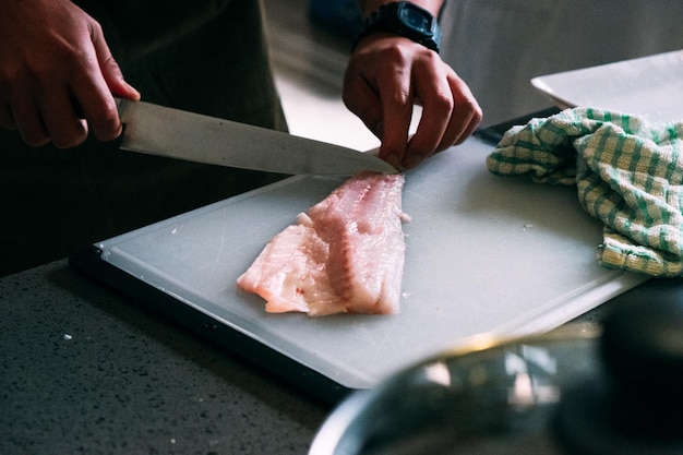 Foto eine person schneidet frischen fisch auf einem schneidbrett in einer küche.