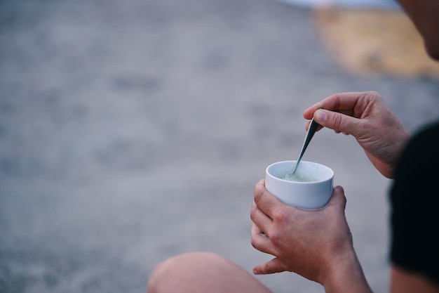 Eine Person sitzt am Strand und hält eine Tasse Tee in der Hand.