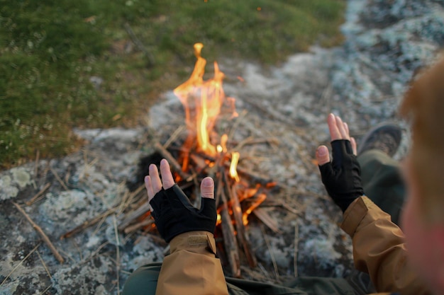 Foto eine person sitzt mit einem handschuh an den händen vor einem lagerfeuer.