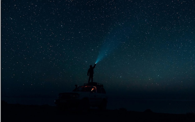 eine Person steht auf einem Jeep mit einer Taschenlampe im Hintergrund